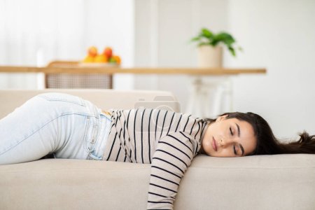 Photo for Tired young pretty arab woman sleep with closed eyes on sofa in light living room interior. Free time, rest, relax, break and lifestyle cozy at home, overwork and insomnia - Royalty Free Image