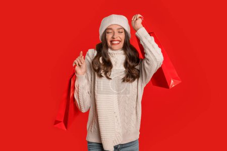 Téléchargez les photos : Offres vacances d'hiver. Happy lady acheteur tient des sacs à provisions posant sur fond de studio rouge, célébrant le début de la vente saisonnière de Noël. Bannière avec dame commerçante joyeuse tenant des achats - en image libre de droit