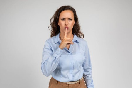 Photo for Strict sad angry young european businesswoman put finger to lips, make shhh sign with hand, isolated on gray studio background. Secret news, gossip and emotions, ad and offer - Royalty Free Image