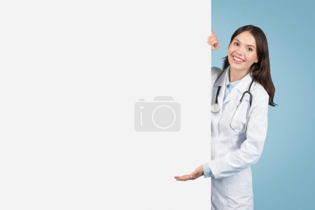 Photo for Young European lady in medical uniform gesturing towards white blank placard board, ideal for medical service offers, free space, mockup - Royalty Free Image