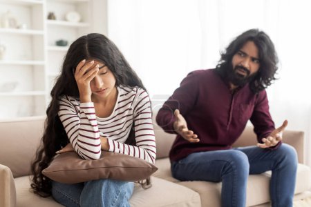 Téléchargez les photos : Breaking Up And Divorce Concept. Jeune couple indien marié se battant, gars criant sur dame pleure, geste à la maison. Homme furieux criant sur sa femme ou sa petite amie, assis sur le canapé au salon - en image libre de droit