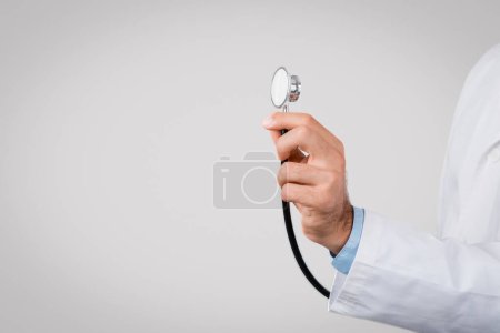 Photo for Focused shot of male medical professionals hand in white coat gripping stethoscope against grey background, symbolizing healthcare and diagnosis - Royalty Free Image