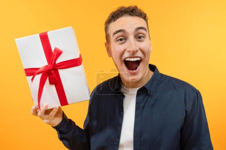 Photo for Gifts and presents. Happy handsome young guy holding wrapped box, feeling excited on yellow studio background. Excited man receiving holiday surprise, celebrating Valentines Day - Royalty Free Image
