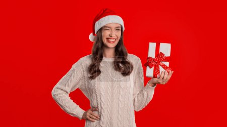 Photo for Winter Gift Delivery. Caucasian Woman Holds Wrapped Present In Box With Bow Standing Over Red Background, Celebrating Christmas Holiday in Studio, Advertising Xmas Offer - Royalty Free Image