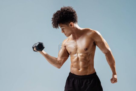 Photo for Athletic young man lifting dumbbells, exercising focused and determined, flexing muscular biceps and strong torso on gray studio backdrop. Fitness and wellness concept - Royalty Free Image