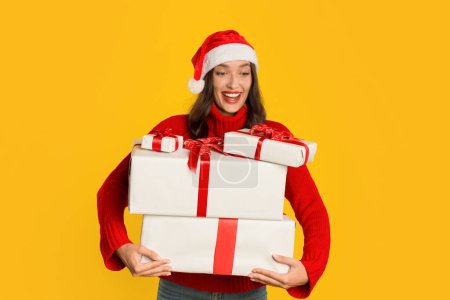 Photo for Excited woman holding many wrapped presents boxes, ready for Christmas holiday gifts giving, standing on yellow studio background, celebrating with smile. Xmas holiday season advertisement - Royalty Free Image