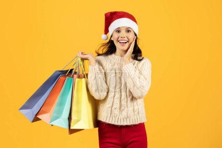 Photo for Excited young Caucasian lady buyer holding paper bags after successful Christmas sale shopping, standing over yellow studio background. New Year celebration and discounts season concept - Royalty Free Image