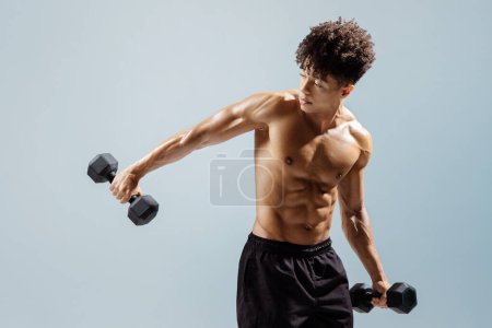 Photo for Sporty Brazilian guy exercising with dumbbells shirtless, strengthening arms muscles, engaging in bodybuilding training over gray studio background. Gym workout and lifestyle banner - Royalty Free Image