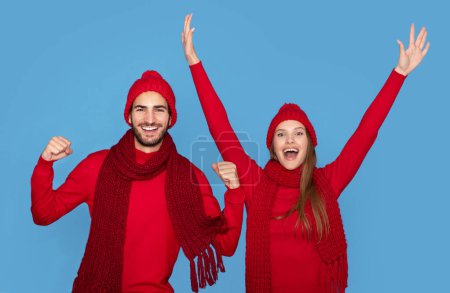 Photo for Holiday Spirit. Portrait Of Overjoyed Young Couple Wearing Winter Hats Celebrating Success, Happy Millennial Spouses Having Fun Together, Posing Isolated Over Blue Studio Background - Royalty Free Image