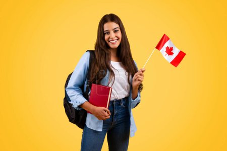 Foto de Feliz mujer estudiante adolescente caucásica, con bandera de Canadá y libro, disfrutar de estudio de intercambio, aislado en el fondo amarillo. Estilo de vida, orgullo nacional y aprendizaje Inglés, Francés - Imagen libre de derechos
