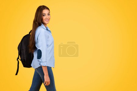 Téléchargez les photos : Heureuse adolescente étudiante européenne avec sac à dos étude, regarder la caméra, profiter d'apprendre, isoler sur fond de studio jaune. Éducation, mode de vie à l'école, publicité et offre - en image libre de droit
