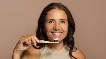Téléchargez les photos : Joyeux caucasien senior femme brossant les dents avec une brosse à dents, profiter de soins buccodentaires, isolé sur fond de studio beige, panorama. Soins dentaires, dentisterie, procédures de routine - en image libre de droit
