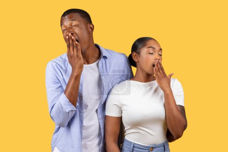 Photo for Fatigued African American young couple yawning in unison, showing signs of exhaustion or boredom, against a vibrant yellow background - Royalty Free Image