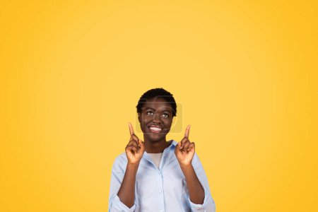 Photo for Smiling young african american woman student in casual points fingers up at copy space, enjoy lesson, isolated on yellow studio background. Study and education, attention sale - Royalty Free Image