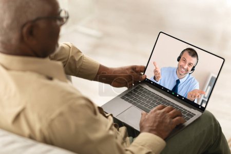 Photo for Back View Of Senior Black Man Using Laptop, Have Video Call With Mature Guy Advisor Or Consultant, Sitting Working Online Indoors. High Angle View. Selective Focus On Display - Royalty Free Image