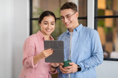 Photo for Smiling young arab lady shows tablet to european man manager in modern coworking office. Startup project app, planning work with device, business together, boss and secretary - Royalty Free Image