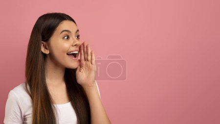 Foto de Emocionada adolescente con su mano cerca de la boca gritando en el espacio de copia, adolescente feliz compartiendo secreto o haciendo anuncio, oferta de publicidad, de pie sobre fondo rosa, panorama - Imagen libre de derechos