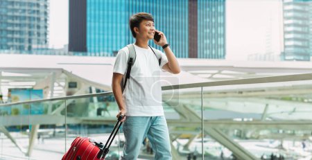 Photo for Roaming Abroad. Handsome Young Asian Man Talking On Cellphone In Airport, Happy Smiling Guy Enjoying Phone Conversation While Waiting For Flight In Terminal, Panorama, Copy Space - Royalty Free Image