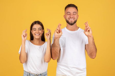 Photo for Cheerful young european man and woman in white t-shirts with crossed fingers hoping or wishing, isolated on yellow studio background. Emotions optimistic and lifestyle, dream come true - Royalty Free Image