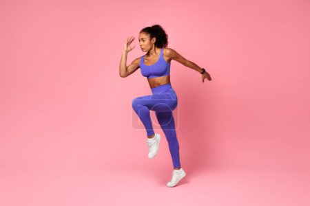 Photo for Athletic African American Lady In Fitwear Jumping Exercising During Training Over Pink Studio Background, Full Length, Side View Shot. Sport Motivation And Fitness Workout Concept - Royalty Free Image