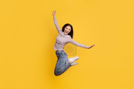 Photo for Carefree joyful pretty young asian woman 20s wearing casual clothing jumping in the air and smiling, posing isolated on yellow studio background, copy space, full length - Royalty Free Image