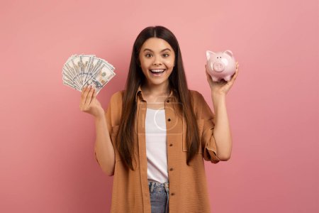 Photo for Joyful teen girl holding piggy bank in hand and fan of cash, happy excited female teenager enjoying money savings, celebrating financial success, standing against vibrant pink background, free space - Royalty Free Image