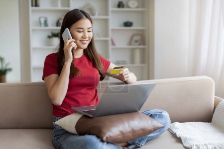 Photo for Smiling asian woman making online purchases via phone with laptop and credit card, smiling young korean female talking to store manager, placing order, enjoying purchasing from internet - Royalty Free Image