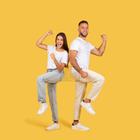 Photo for Glad young european man and woman in white t-shirts celebrate victory together, success gesture with fists up, isolated on yellow studio background. Emotions, good news, sale - Royalty Free Image