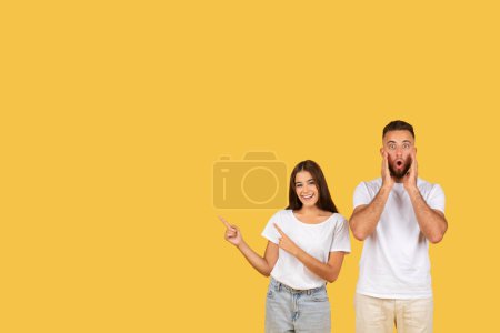 Photo for Glad shocked young european man with open mouth, woman in white t-shirts point finger at copy space, isolated on yellow studio background. Emotions, surprise attention good news, sale - Royalty Free Image