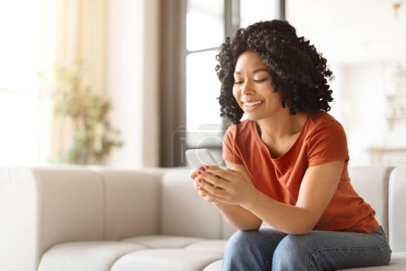 Photo for Portrait Of Young Black Woman Using Mobile Phone At Home, Happy Smiling African American Lady Shopping Online On Smartphone Or Texting With Friends, Browsing New App While Relaxing On Couch - Royalty Free Image