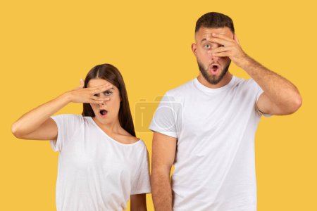 Téléchargez les photos : Humour mécontent jeune femme européenne triste et mari en t-shirts blancs couvre nez avec les mains, souffrent de mauvaise odeur, isolé sur fond de studio jaune. Expressions dégoûtantes - en image libre de droit