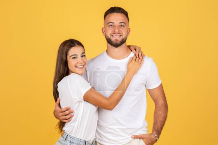 Photo for Happy young european couple in white t-shirts, enjoy romantic date together, hugs, isolated on yellow studio background. Ad and offer, sale and lifestyle, relationships and love - Royalty Free Image
