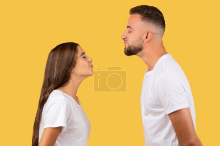 Photo for Happy young european man and woman in white t-shirts, enjoy romantic date together, kiss, isolated on yellow studio background, profile. Lifestyle, relationships and love - Royalty Free Image