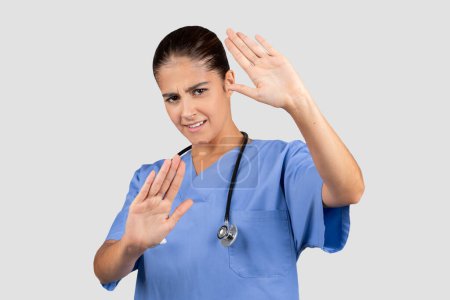 Photo for Unhappy european young doctor, nurse in blue uniform make stop gesture, keeping hands to defend, protect herself, isolated on gray background, panorama. Health care, medicine - Royalty Free Image