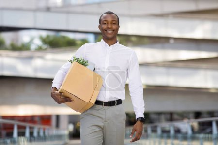 Photo for Happy Black Man In Shirt Carrying Box With Personal Belongings While Walking Outdoors, Smiling African American Man Got Job, Going To New Office, Looking At Camera, Enjoying Career Promotion - Royalty Free Image