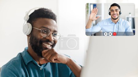 Téléchargez les photos : Gros plan de l'homme noir joyeux ont chat vidéo avec représentant du soutien technique Moyen-Orient jeune homme. Support technique d'appel client heureux, utilisant l'ordinateur et les écouteurs sans fil - en image libre de droit