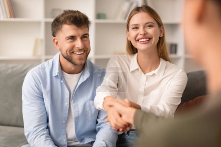 Photo for Thankful young couple warmly shake hands with their counselor seated on couch in therapists office, expressing gratitude for professional guidance that helped their relationship - Royalty Free Image