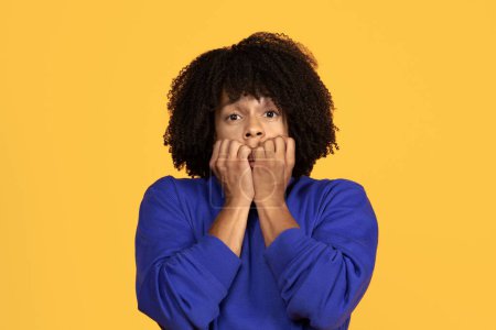 Photo for Anxious young black guy biting his nails and looking at camera, scared millennial african american man feeling worried, having panic attack, standing isolated on yellow studio background, copy space - Royalty Free Image