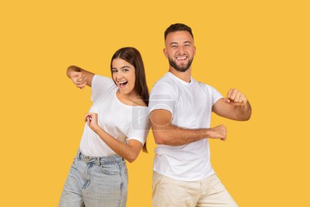 Photo for Glad young european guy and lady in white t-shirts have fun, enjoy free time, isolated on yellow studio background. Emotions and lifestyle, dance at music, party together - Royalty Free Image