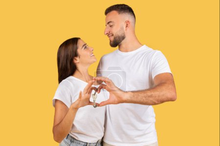 Photo for Positive romantic millennial european family in white t-shirts hugs, making heart gesture with hands, enjoy spare time, isolated on yellow studio background. Emotions love, date and lifestyle - Royalty Free Image