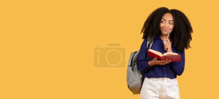 Téléchargez les photos : Dame noire pensive avec sac à dos tenant livre et stylo, contemplant, tout en se tenant sur fond jaune, incarnant la curiosité académique - en image libre de droit