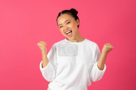 Photo for Portrait Of Joyful Asian Woman Celebrating Success While Standing On Pink Studio Background, Happy Young Korean Female Shaking Fists And Exclaiming With Excitement, Cheering Big Luck, Copy Space - Royalty Free Image