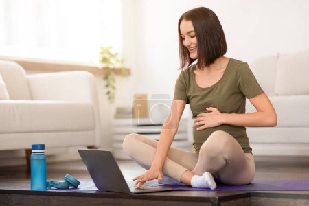 Photo for Young pregnant lady practices prenatal yoga using computer at home, browsing laptop during training for online guidance, focusing on wellbeing and fitness during pregnancy. Sport and health - Royalty Free Image