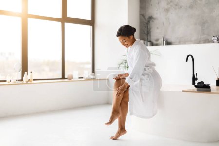 Photo for Happy African American Lady Applying Moisturizer Cream On Legs, Caring For Body And Moisturizing Skin After Shaving, Smiling Black Woman Sitting On Bathtub In Luxury Bathroom At Home, Copy Space - Royalty Free Image