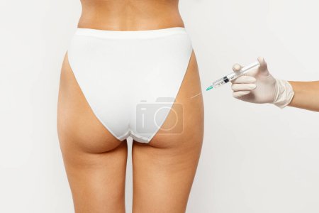 Photo for Professional beauty surgeon in gloves make injection to millennial lady for plastic surgery operation, isolated on gray studio background, back. Treatment, weight loss, doctors help, body care - Royalty Free Image