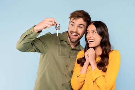 Téléchargez les photos : Délicieux jeune homme affichant fièrement une nouvelle clé de voiture avec une femme ravie, célébrant leur récent achat ensemble sur un fond bleu - en image libre de droit