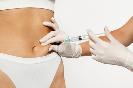 Photo for A gloved medical professional is carefully administering subcutaneous injection in abdomen area of european millennial lady wearing white underwear. Health care and medical procedure, weight loss - Royalty Free Image