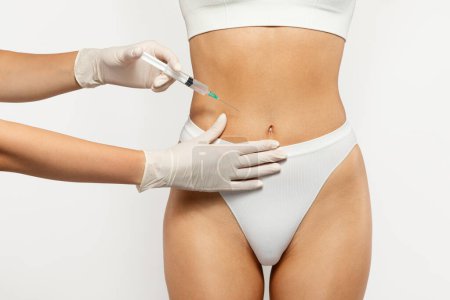 Photo for Close up of health care professional in gloves administering injection at belly of young european lady in white underwear. Health and medical treatment, weight loss, surgery and beauty care - Royalty Free Image