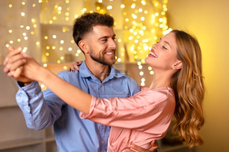 Foto de La feliz pareja comparte el baile en una habitación cálidamente iluminada, sus sonrisas expresando la alegría y el amor de un momento especial juntos, en un contexto de luces centelleantes - Imagen libre de derechos