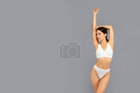 Téléchargez les photos : Femme millénaire asiatique calme en sous-vêtements blancs profiter de temps libre, soins du corps, peau douce sèche, isolé sur fond de studio gris. Soins de beauté et bien-être, journée spa, propreté - en image libre de droit
